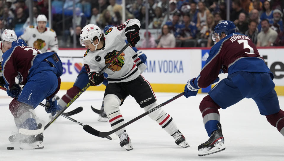 Chicago Blackhawks center Connor Bedard, center, fights to control the puck as Colorado Avalanche defenseman Jack Johnson, right, covers in the second period of an NHL hockey game Thursday, Oct. 19, 2023, in Denver. (AP Photo/David Zalubowski)