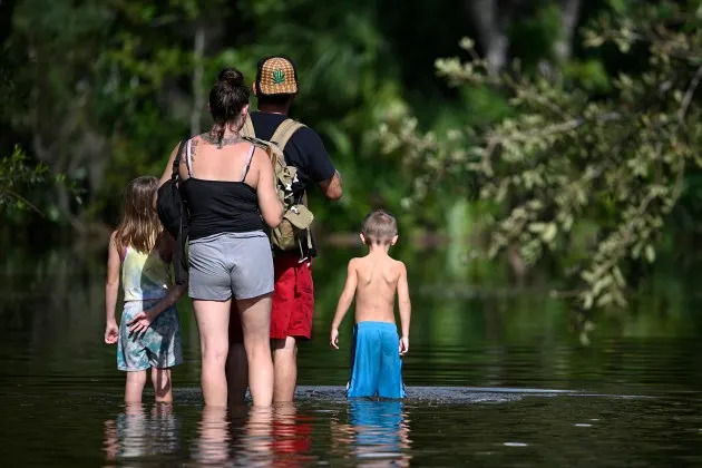 A *real* Florida family walking through floodwaters as they return home after Hurricane Helene. - Credit: AP