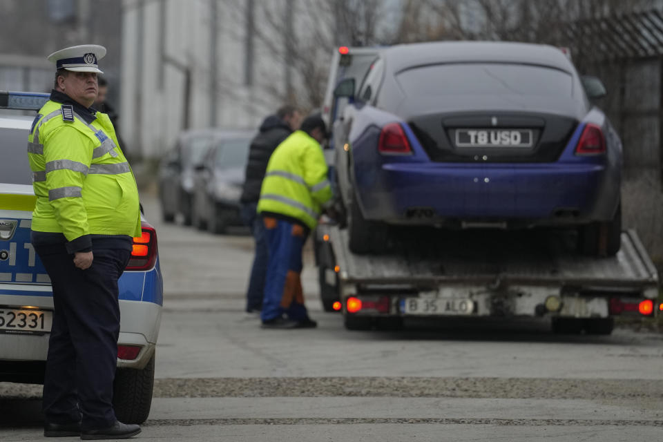 A Romannian traffic policeman stands by as men secure a UK registered luxury vehicle which was seized in a case against media influencer Andrew Tate, is towed away, on the outskirts of Bucharest, Romania, Saturday, Jan. 14, 2023. Prosecutors seized several luxury vehicles after Tate lost a second appeal this week at a Bucharest court, where he challenged the seizure of assets in the late December raids, including properties, land, and a fleet of luxury cars. More than 10 properties and land owned by companies registered to the Tate brothers have also been seized so far. (AP Photo/Vadim Ghirda)