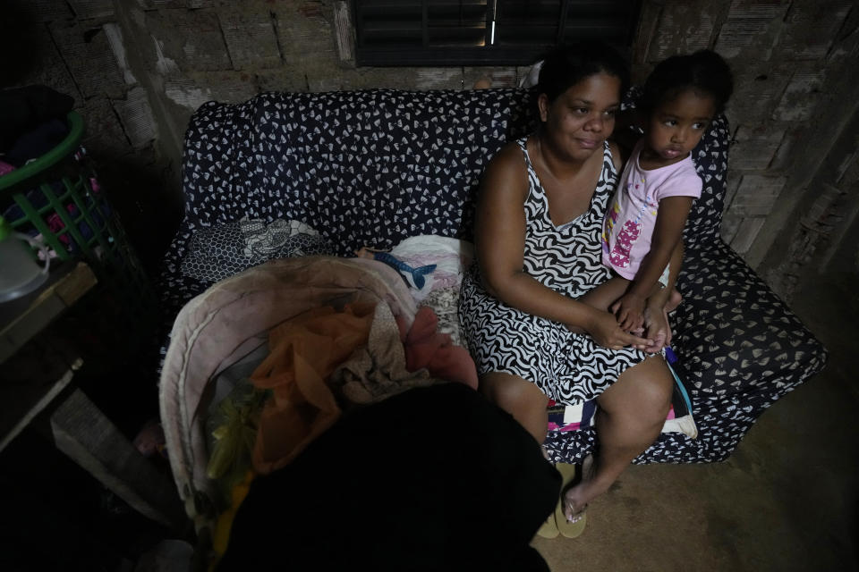 Nayara Miguel and her daughter sit inside their home in the Sol Nascente favela of Brasilia, Brazil, Wednesday, March 22, 2023. Miguel is a housewife with two kids in an area of Sol Nascente that now has electricity and water, and where the local government recently paved streets and installed public lighting. (AP Photo/Eraldo Peres)