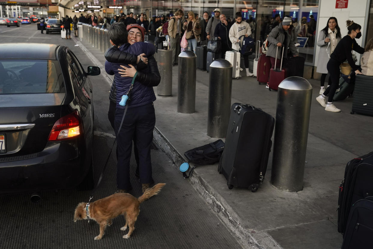 Two people hug outside a terminal as travelers wait in line to check in at Los Angeles International Airport in Los Angeles, Monday, Dec. 19, 2022. (AP Photo/Jae C. Hong)