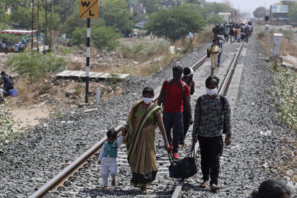 In this Monday, May 11, 2020, photo, migrant workers from other states desperate to return to their homes walk through rail tracks towards a train station in Ahmedabad, India. Tens of thousands of impoverished migrant workers are on the move across India, walking on highways and railway tracks or riding trucks, buses and crowded trains in blazing heat amid threat to their lives from the coronavirus pandemic. (AP Photo/Ajit Solanki)