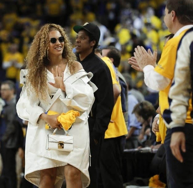 Beyonce waving goodbye at a basketball game with Jay Z behind her