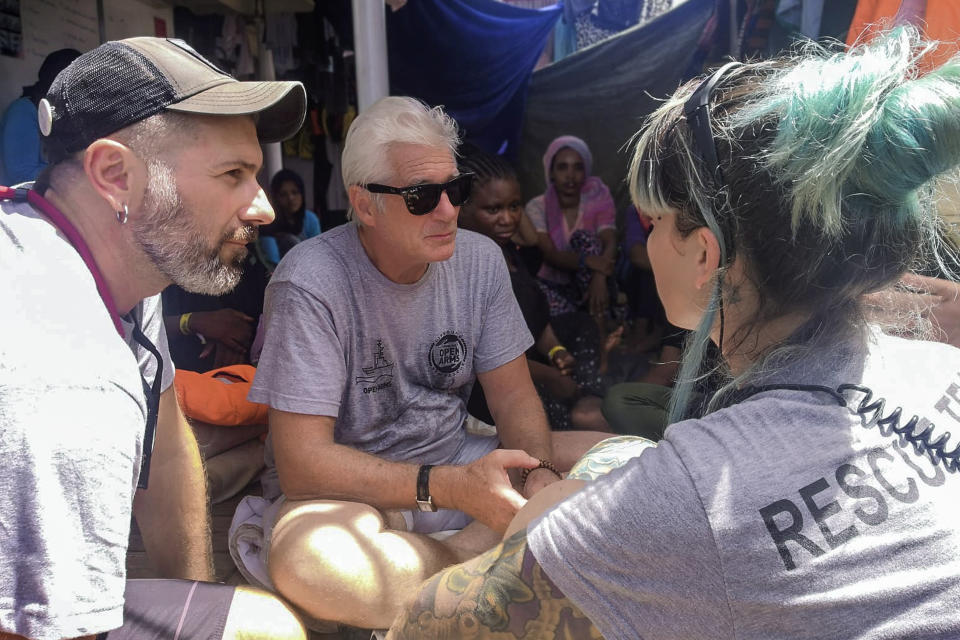 Actor Richard Gere, center, talks with staff members of the Open Arms Spanish humanitarian boat as it cruises in the Mediterranean Sea, Friday, Aug. 9, 2019. Open Arms has been carrying 121 migrants for a week in the central Mediterranean awaiting a safe port to dock, after it was denied entry by Italy and Malta. (AP Photo/Valerio Nicolosi)