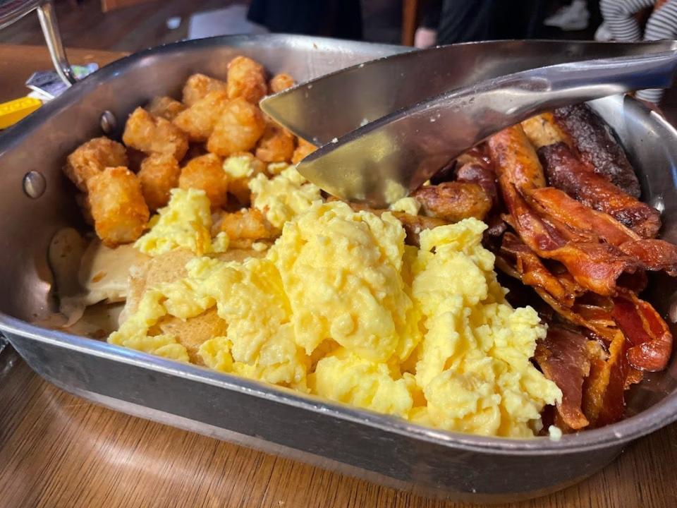 Eggs, tater tots, and bacon in a silver dish.