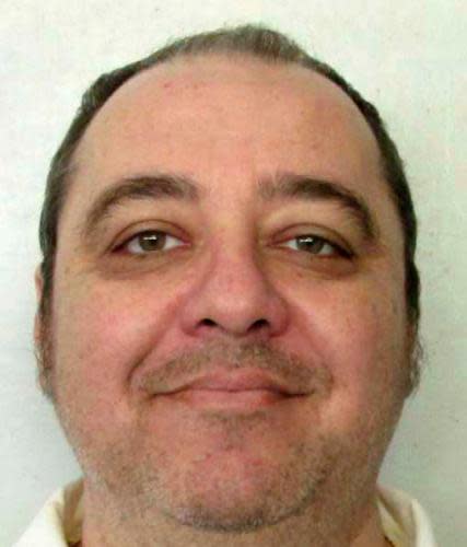 A mug shot of a smiling, middle-aged, balding white man, whose brown hair is combed back from the crown of his head. He has stubble and appears to be wearing a white-collared shirt.