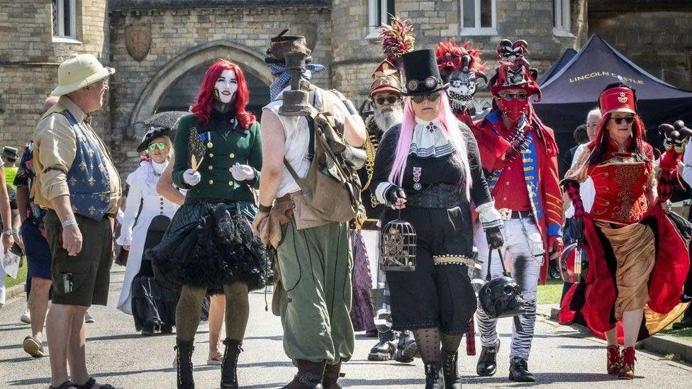 Steampunks walking through Lincoln's historic quarter. Outfits range from black to red, with some wearing brightly-coloured wigs, or top hats and goggles