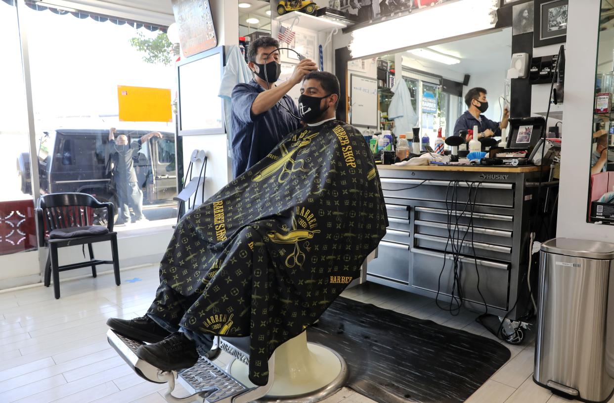 A barber and his client wear face masks in the Hollywood Barber Shop shortly before closing amid new restrictions due to the COVID-19 pandemic on July 13, 2020, in Los Angeles, Calif. California Governor Gavin Newsom announced updated restrictions including a statewide closure of bars, indoor dining, zoos, malls and museums following a surge in the spread of the coronavirus. In addition, most counties including Los Angeles county must shutter worship services, gyms, hair salons, barbershops and some other businesses.