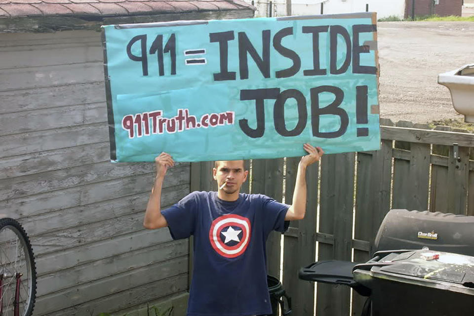 In this 2006 photo provided by Hector Tapia Perez Jr., his brother, Antonio Perez, holds a sign which reads "911 = Inside Job!" in Detroit. "I fully bought into the lie that it was an inside job. I had watched (the documentary series) "Loose Change." I watched a bunch of Alex Jones documentaries. ... I think that was the last conspiracy I started to fall out of. Even up until like maybe 2012, there still parts of me that that almost believed it." (Hector Tapia Perez Jr. via AP)