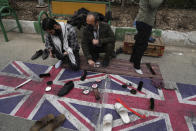 A man polishes shoes of worshippers on the images of the British flag during Friday Prayers ceremony in Tehran, Iran, Friday, Jan. 27, 2023. (AP Photo/Vahid Salemi)