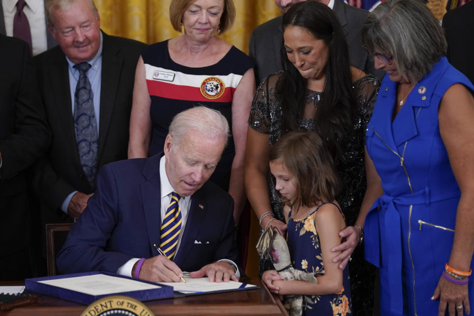 FILE - Danielle and Brielle Robinson, the wife and daughter of Sgt. 1st Class Heath Robinson, who died of cancer two years ago watch as President Joe Biden signs the "PACT Act of 2022" during a ceremony in the East Room of the White House, Wednesday, Aug. 10, 2022, in Washington. Hundreds of thousands of veterans have received additional benefits in the past year after Biden signed legislation expanding coverage for conditions connected to burn pits that were used to destroy trash and potentially toxic materials. (AP Photo/Evan Vucci, File)