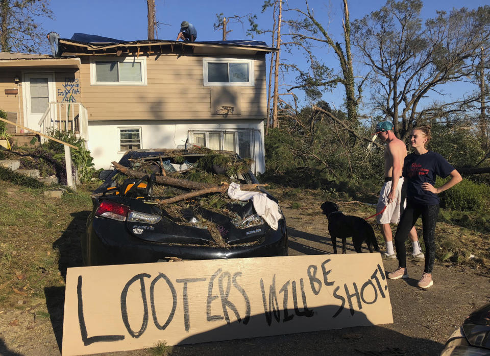 In this Oct. 10, 2018 photo Shauna Benefield and Alex Edwards stand near a sign warning looters in front of their house in Marianna, Fla., which was damaged by fallen trees during Hurricane Michael. Armed looters are targeting homes and businesses that remain without electricity after being ravaged by Hurricane Michael a week ago. (AP Photo/Brendan Farrington)