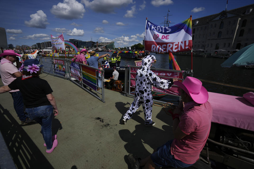 Police, rear, prevented protetesting farmers from taking part in the Pride Canal Parade as thousands of people lined canals in the Dutch capital to watch the colorful spectacle of the 25th edition after the last two events were canceled due to the COVID-19 pandemic, in Amsterdam, Netherlands, Saturday, Aug. 6, 2022. (AP Photo/Peter Dejong)