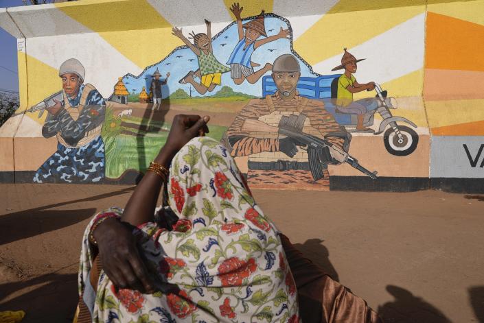 A woman looks at a mural depicting children playing with armed military soldiers nearby.