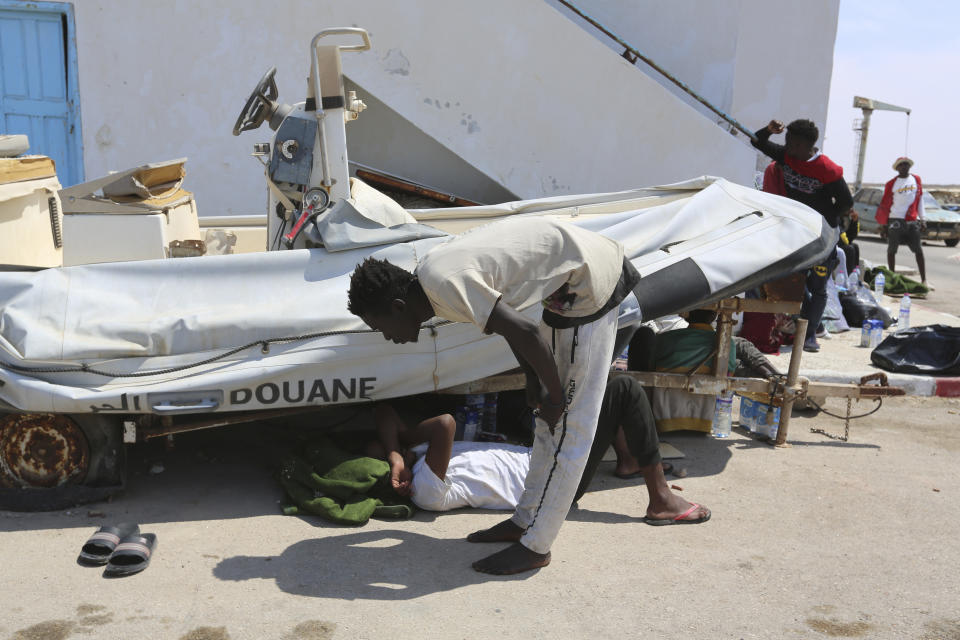 A migrant rests under a Tunisian custom boat in Ben Guerdane, southern Tunisia, Saturday June 12, 2021. Since the beginning of the year, over 600 people have died on the stretch of central Mediterranean coastline from Libya into Tunisia trying to reach Europe, according to the International Organization for Migration. (AP Photo/Mehdi El Arem)