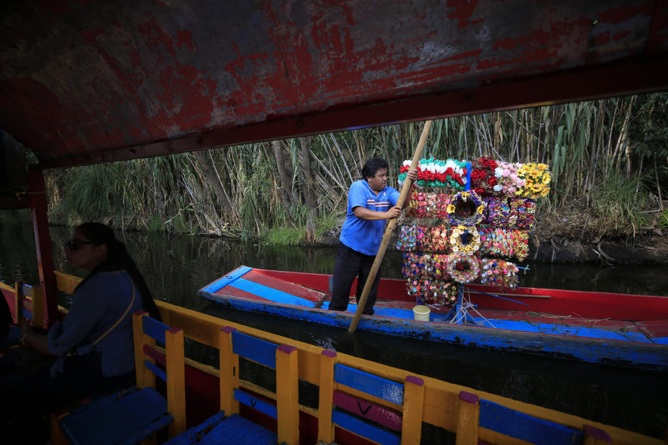 A flower crown vendor markets his wares next to a sparsely-occupied trajinera, colorful passenger boats typically rented by tourists, families, and groups of young people, in Xochimilco, Mexico City, Friday, Sept. 6, 2019. The usually festive Nativitas pier was subdued and largely empty Friday afternoon, with some boat operators and vendors estimating that business was down by 80% on the first weekend following the drowning death of a youth that was captured on cellphone video and seen widely in Mexico. Borough officials stood on the pier to inform visitors of new regulations that went into effect Friday limiting the consumption of alcohol, prohibiting the use of speakers and instructing visitors to remain seated.(AP Photo/Rebecca Blackwell)