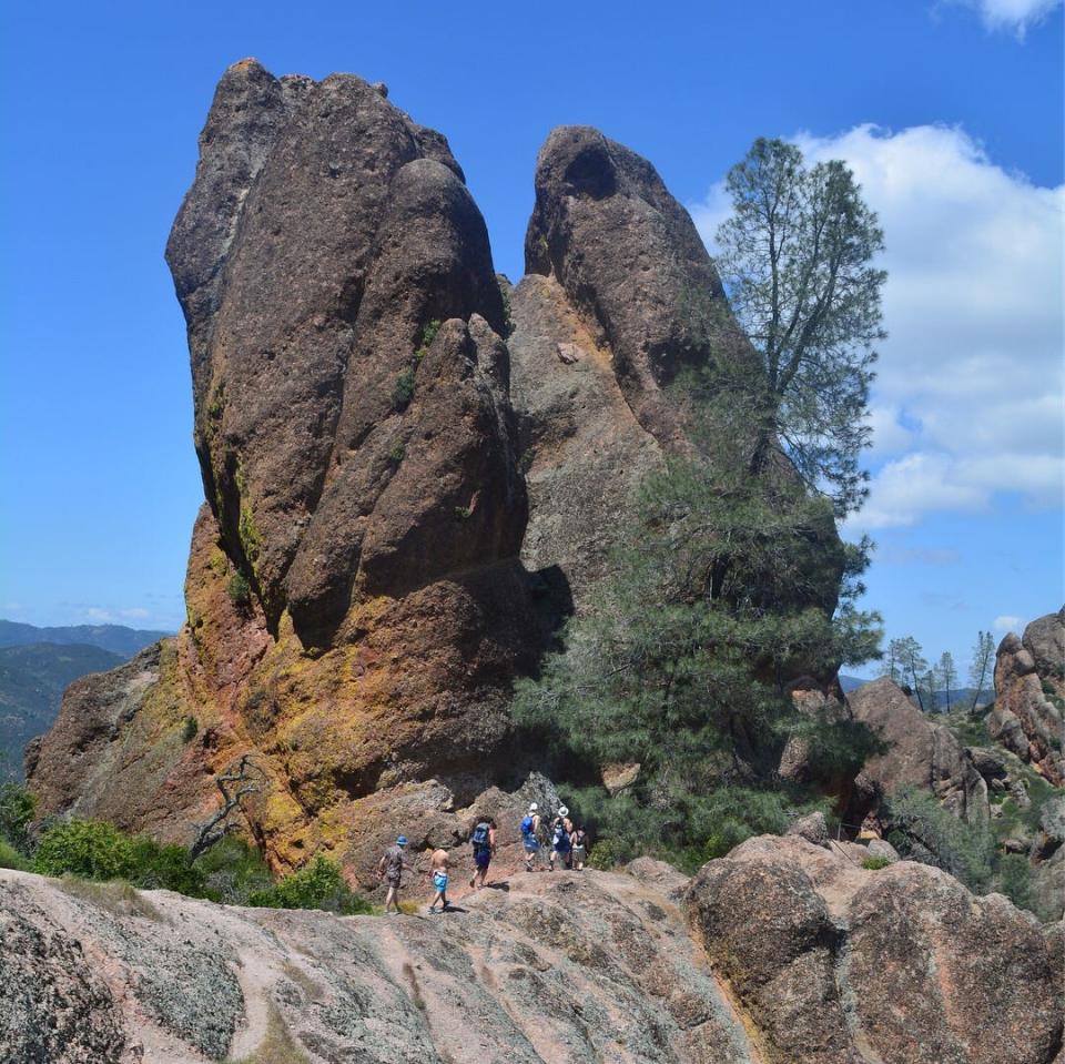 A group of people hike on and in front of gigantic rocks with blue skies in the background.