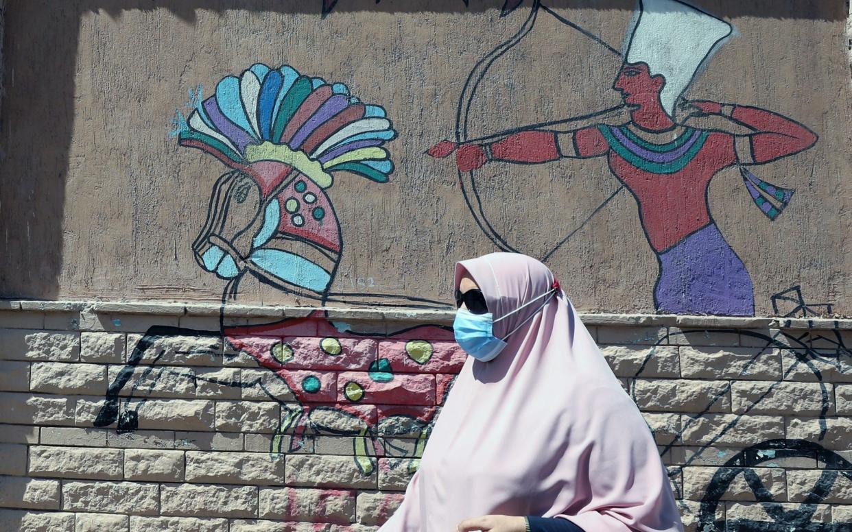 A woman wearing protective face mask walks near wall painting on a street in Cairo, Egypt - Khaled Elfiqi