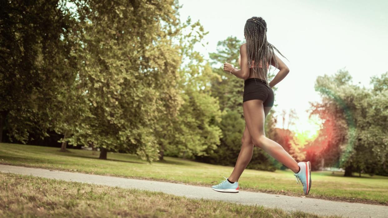  A woman running through a park in running shorts and a sports bra. 