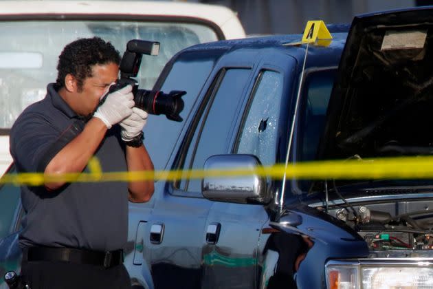 A crime scene investigator from the Los Angeles County Sheriff's Department photographs the window of a black SUV in which a fatal gunshot victim was found.