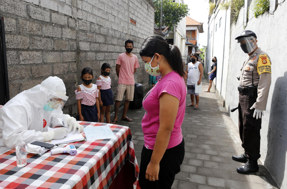 Un trabajador sanitario comprueba la identificación de los vecinos, meintras esperan para hacerse una prueba de anticuerpos de coronavirus en un poblado de Bali, Indonesia, el miércoles 27 de mayo de 2020. (AP Foto/Firdia Lisnawati)