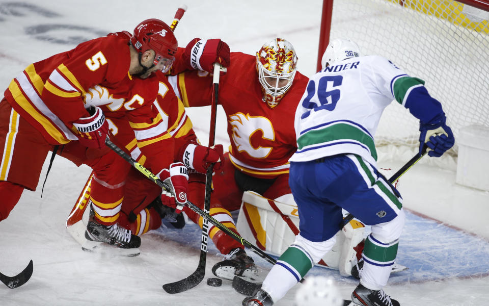 Vancouver Canucks' Nils Hoglander, right, scrambles for the puck in front of Calgary Flames goalie Jacob Markstrom, center, and Flames' Mark Giordano during the first period of an NHL hockey game Saturday, Jan. 16, 2021, in Calgary, Alberta. (Jeff McIntosh/The Canadian Press via AP)