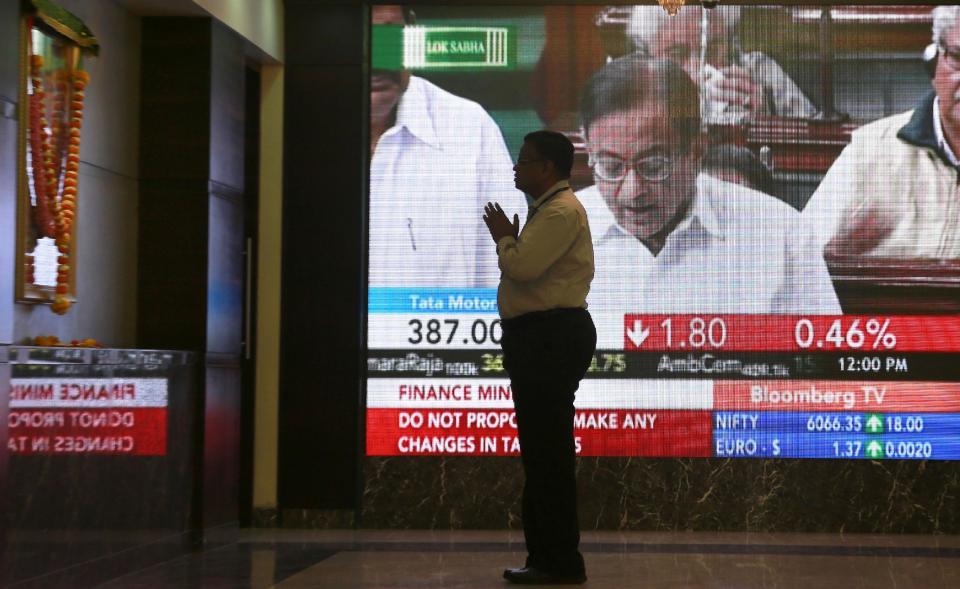 A man offers prayer standing in front of a photograph of a Hindu goddess at the Bombay Stock Exchange (BSE) office as India's Finance Minister P. Chidambaram is seen on a television screen presenting interim budget for the fiscal year 2014-15, in Mumbai, India, Monday Feb. 17, 2014. India's finance minister has unveiled a conservative budget for the government’s remaining time in office through May in parliament. (AP Photo/Rafiq Maqbool)