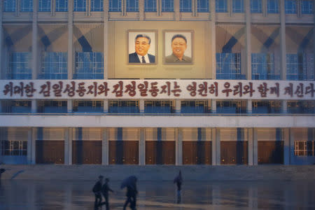 People pass in front of the building decorated with slogan "The great comrades Kim Il Sung and Kim Jong Il will be with us forever" and their pictures in central Pyongyang, May 3, 2016. REUTERS/Damir Sagolj
