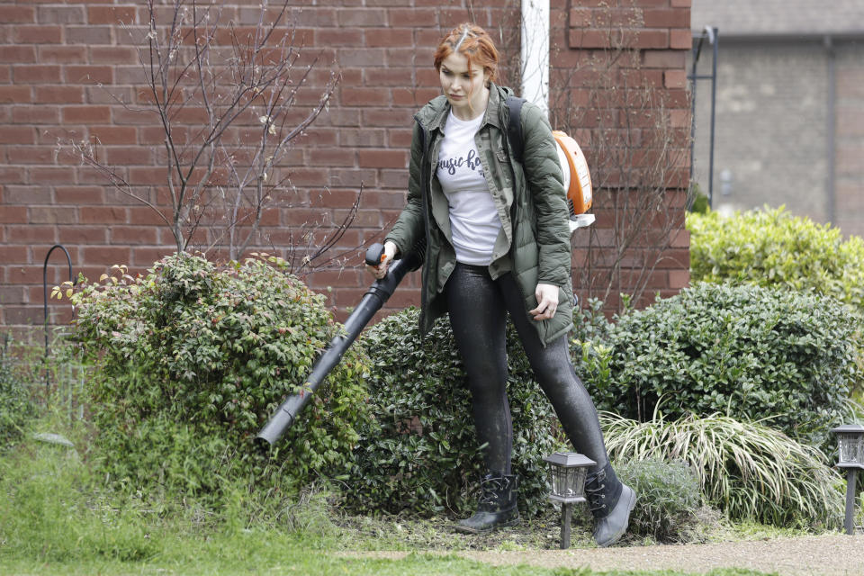 In this March 25, 2020, photo, country singer Caylee Hammack uses a leaf blower to clear a sidewalk as she does landscaping work in Mt. Juliet, Tenn. Hammack's band was facing months without income after their touring schedule was wiped clean due to the spreading coronavirus, so they started a side gig landscaping to keep bills paid. (AP Photo/Mark Humphrey)