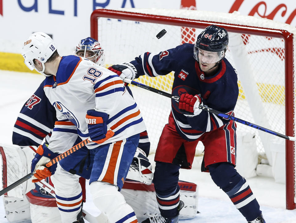 Winnipeg Jets goaltender Connor Hellebuyck (37) watches the puck as Josh Morrissey (44) defends against Edmonton Oilers' Zach Hyman (18) during the first period of an NHL hockey game Tuesday, March 26, 2024, in Winnipeg, Manitoba. (John Woods/The Canadian Press via AP)