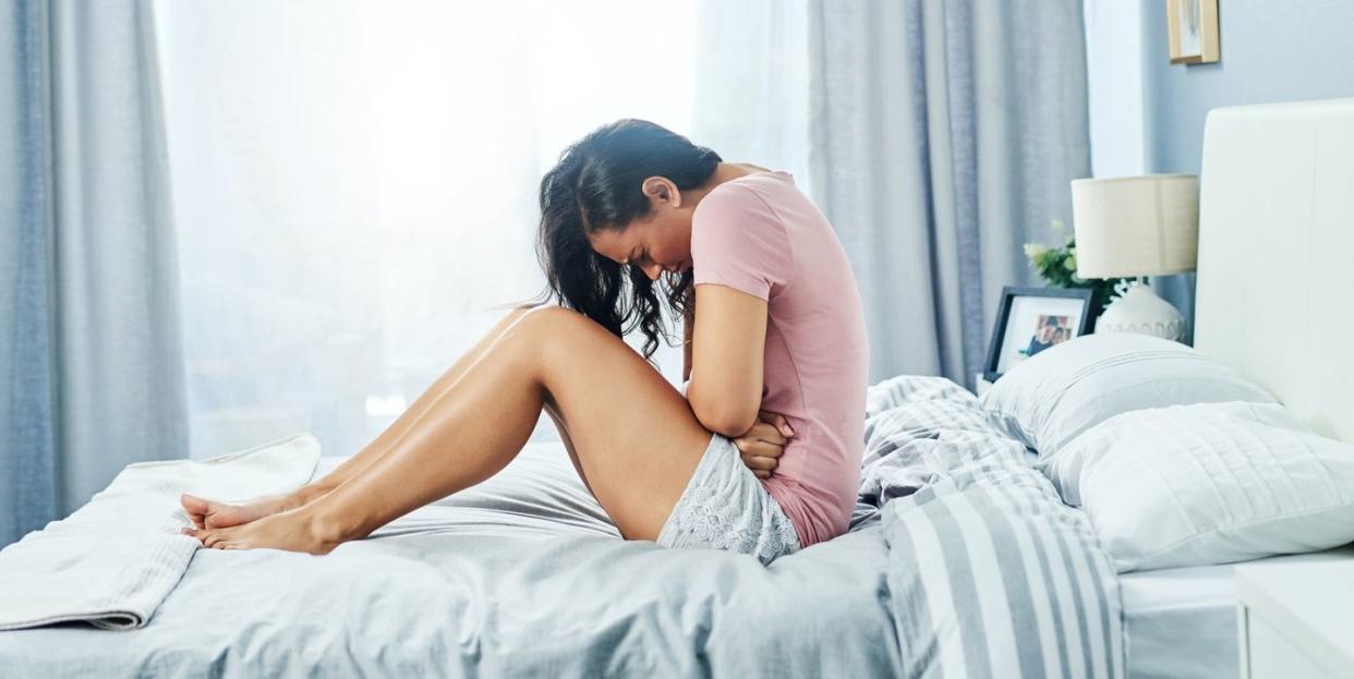 shot of an uncomfortable looking young woman suffering from stomach cramps in her bedroom