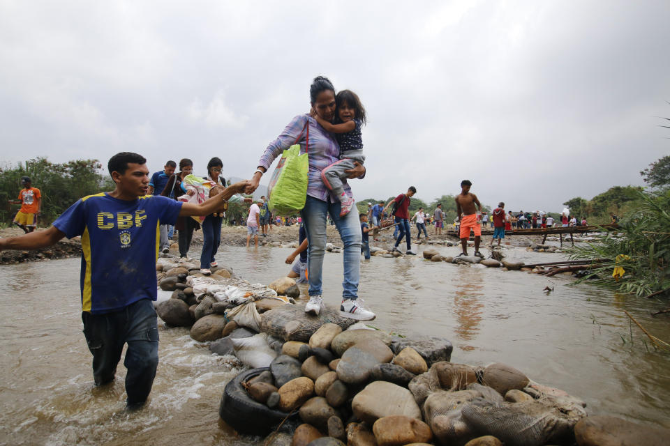 A woman carrying a crying girl holds a man's hand to help her across a makeshift bridge in Tachira River into Colombia near the Simon Bolivar International bridge, which Venezuelan authorities only open to students and the sick, in Cucuta, Colombia, Tuesday, March 12, 2019, on the border with Venezuela. People crossing the river are using makeshift bridges as the water level grows with the approaching rainy season, with some paying a small tip to people who help them cross without getting wet. (AP Photo/Schneyder Mendoza)