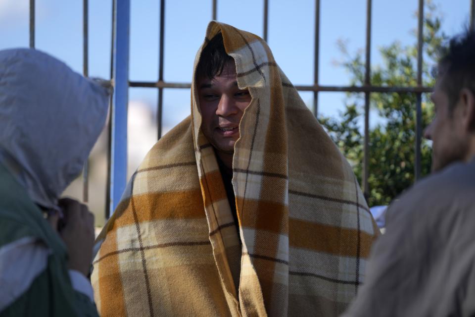 An Afghan covered with a blanket, speaks with other migrants at an old school used as a temporary shelter on the island of Kythira, southern Greece, Friday, Oct. 7, 2022. Strong winds were hampering rescue efforts at two Greek islands Friday for at least 10 migrants believed to be missing after shipwrecks left more than 20 people dead, officials said. (AP Photo/Thanassis Stavrakis)