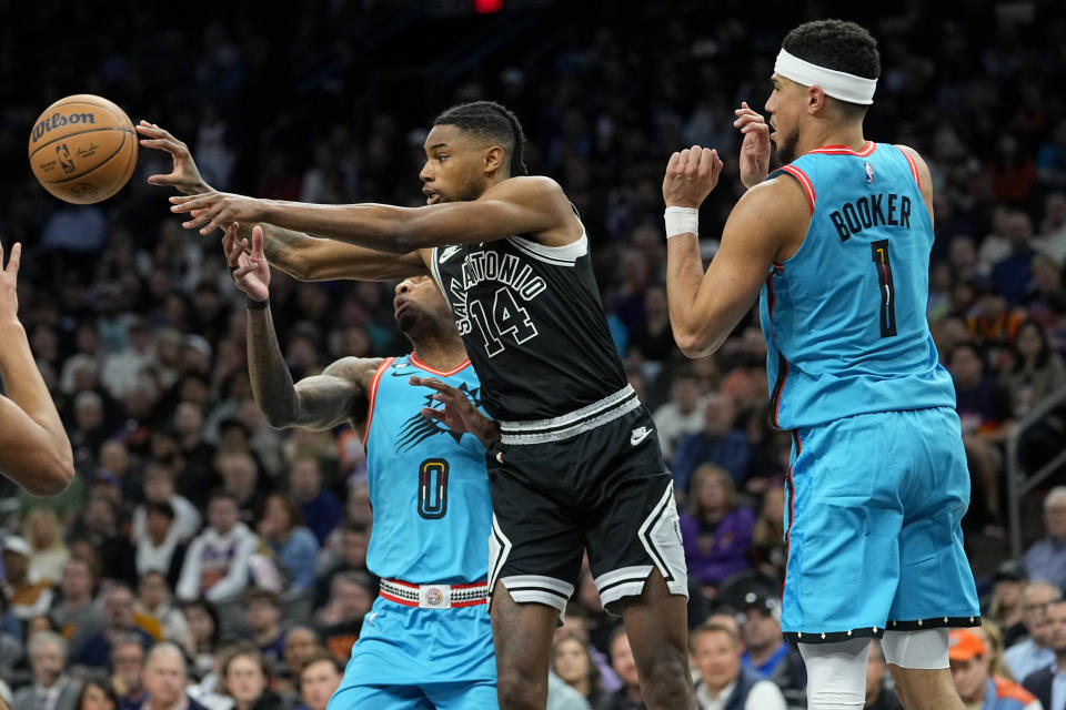 San Antonio Spurs guard Blake Wesley (14) dishes off as Phoenix Suns forward Torrey Craig (0) and guard Devin Booker (1) defend during the first half of an NBA basketball game, Tuesday, April 4, 2023, in Phoenix. (AP Photo/Matt York)