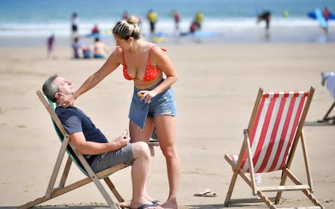 Sunbathers apply sunscreen during the hot sunshine on Towan beach in Newquay, Cornwall - Credit: PA