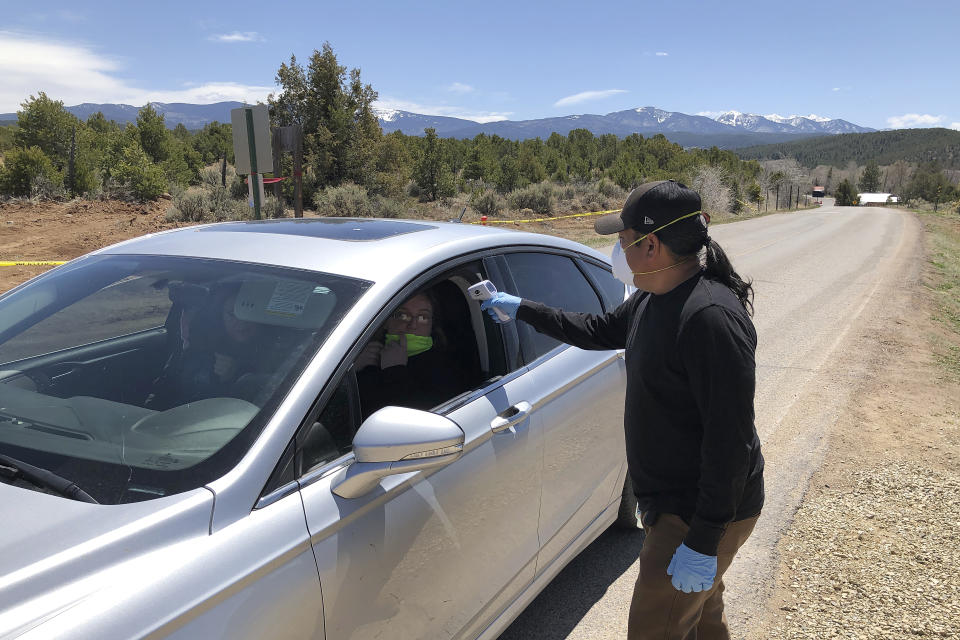 Members of the Native American community of Picuris Pueblo, N.M., including Vaughn Tootsie, right, screens vehicles as they enter and exit tribal property Thursday, April 23, 2020. Pueblo leaders including Gov. Craig Quanchello see COVID-19 as a potentially existential threat to the tribe of roughly 300 members and have implemented universal testing for infection. (AP Photo/Morgan Lee)