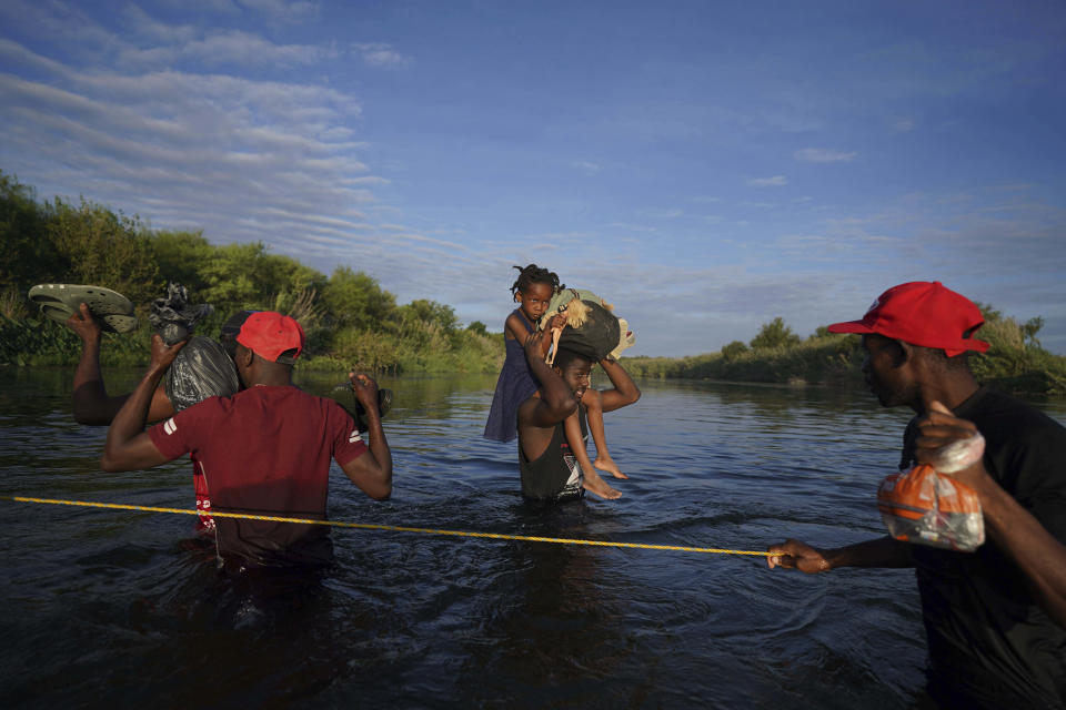 A man carries a little girl, who is clutching her Barbie doll, over the Rio Grande river toward Del Rio, Texas, early Wednesday, Sept. 22, 2021, as other migrants return to Ciudad Acuna, Mexico, some to avoid possible deportation from the U.S. and others to load up with supplies. (AP Photo/Fernando Llano)