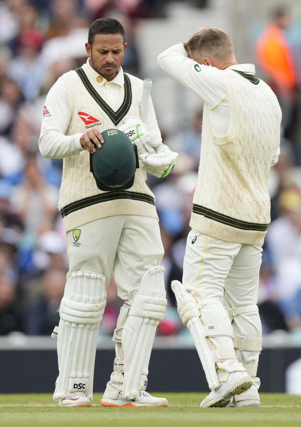 Australia's Usman Khawaja, left, inspects his helmet with Australia's David Warner after he is hit by the ball on day four of the fifth Ashes Test match between England and Australia, at The Oval cricket ground in London, Sunday, July 30, 2023. (AP Photo/Kirsty Wigglesworth)