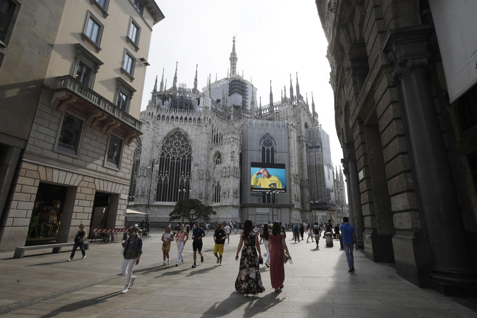 Pedestrians pass by a screen on the Duomo cathedral, showing a Moschino model during the Milan Digital Fashion Week, in Milan, Italy, Tuesday, July 14, 2020. Forty fashion houses are presenting previews of menswear looks for next spring and summer and pre-collections for women in digital formats, due to concerns generated by the COVID-19. (AP Photo/Luca Bruno)