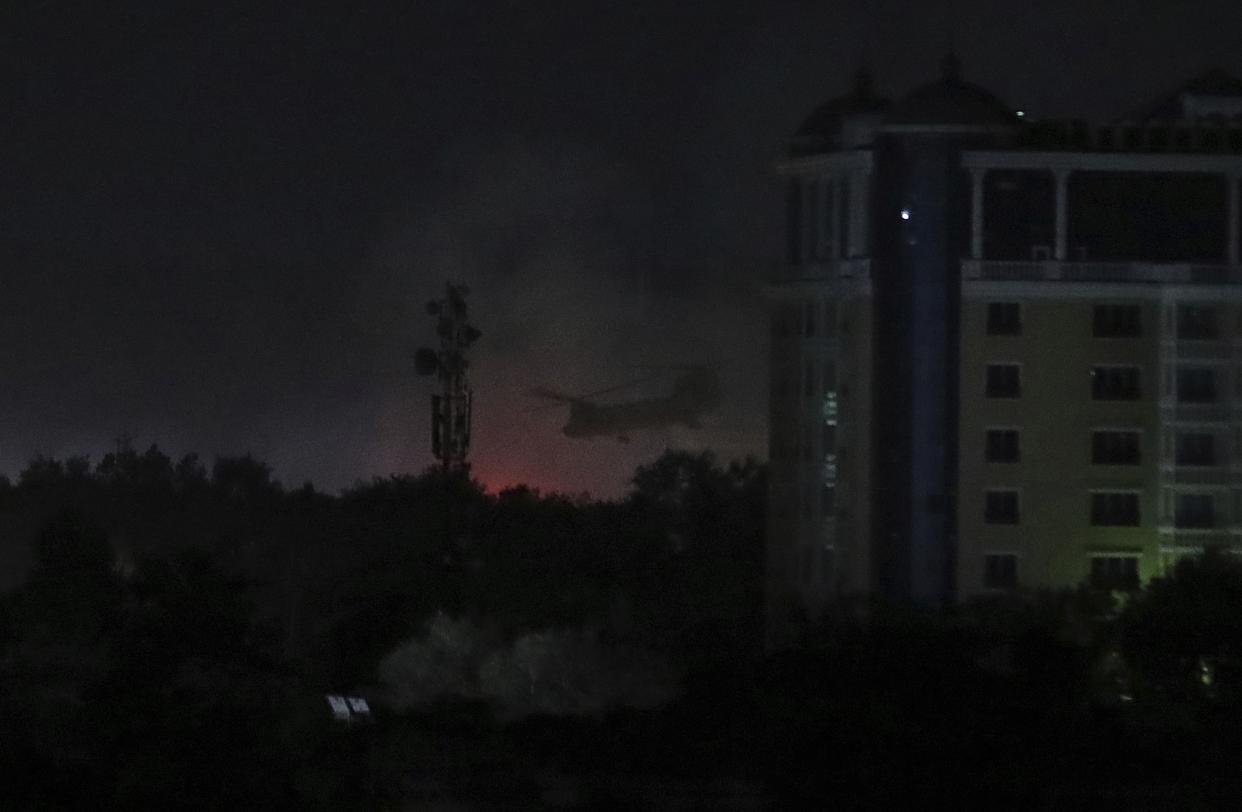 A U.S. Chinook helicopter flies near the U.S. Embassy as smoke rises in Kabul, Afghanistan, late Sunday, Aug. 15, 2021.