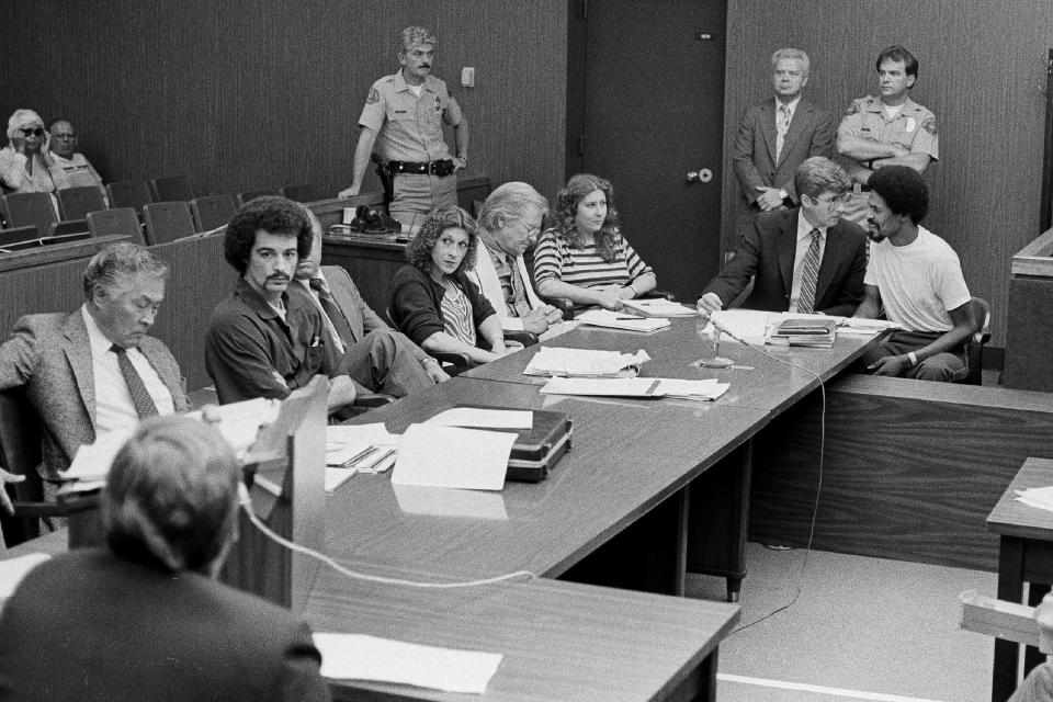 FILE - In this Aug. 22, 1983, file photo, four persons charged in connection with the June 2, 1983, fatal shooting of Los Angeles Police Officer Paul Verna sit with their attorneys during a preliminary hearing in a San Fernando, Calif., courtroom. Seated second from left to right, Kenneth Gay, an unidentified attorney, Robin Gay, attorney Elmer Docken, Pam Cummings, attorney Edward Rucker and Reynard Cummings. Prosecutors will re-try the case against Gay, but have not yet decided if they will seek the death penalty again. The California Supreme Court has twice overturned Gay's death penalty sentence and in February 2020 vacated his original conviction, forcing the Los Angeles County District Attorney's office to decide if it would pursue the case again. (AP Photo/Michael Tweed, File)