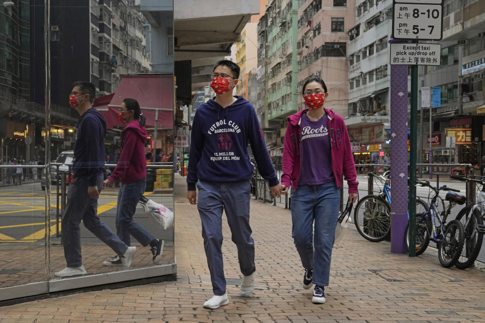 People wearing face masks walk alone a street in Hong Kong, Sunday, March 13, 2022. The territory's leader, Chief Executive Carrie Lam, warned the peak of the latest surge in coronavirus infections might not have passed yet. (AP Photo/Kin Cheung)