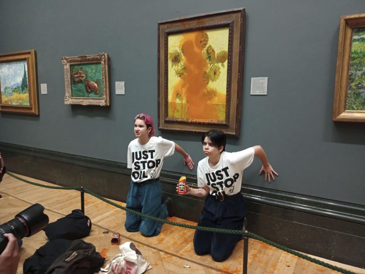 A handout photo issued by Just Stop Oil of two protesters who have thrown tinned soup at Vincent Van Gogh's famous 1888 work Sunflowers at the National Gallery in London, Friday Oct. 14, 2022. 