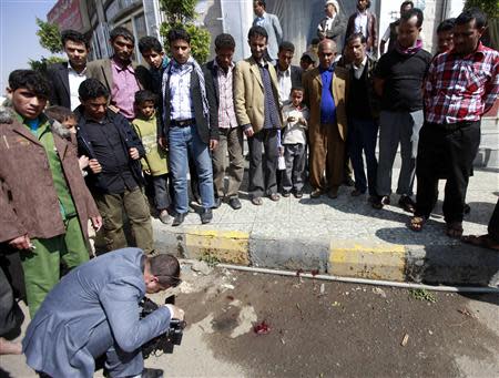 People look on as a cameraman films blood stains left behind after two Russian military instructors were shot dead in front of Hotel Amsterdam on Benon street in Sanaa, November 26, 2013. REUTERS/Mohamed al-Sayaghi