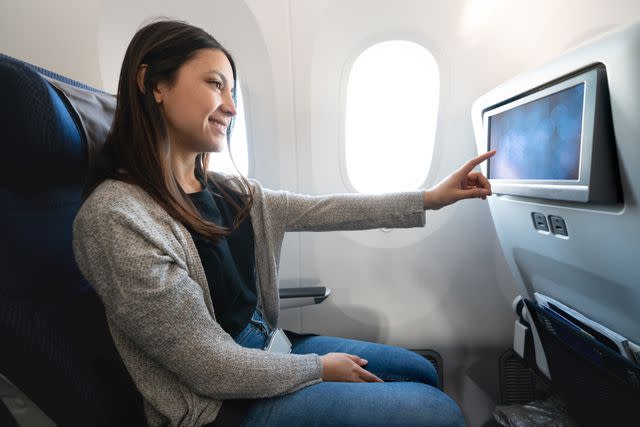 <p>Getty</p> Stock image of a woman selecting something on her screen on the airplane