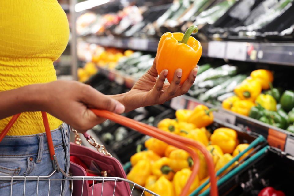 Mixed race, African young woman shopping in supermarket, holding a yellow pepper