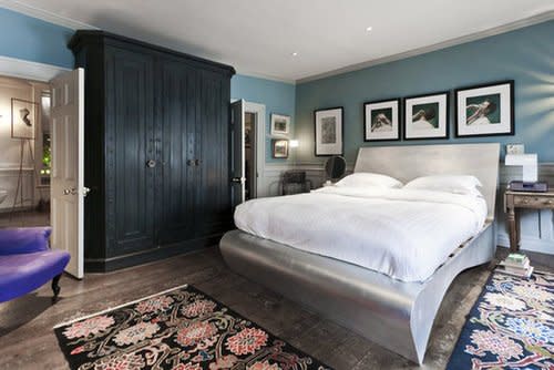 The master bedroom of this London home features a silvered super-king-size bed. A formidable antique wardrobe rests against one wall but is given levity, thanks to the fun floral rugs. Source: One Fine Stay