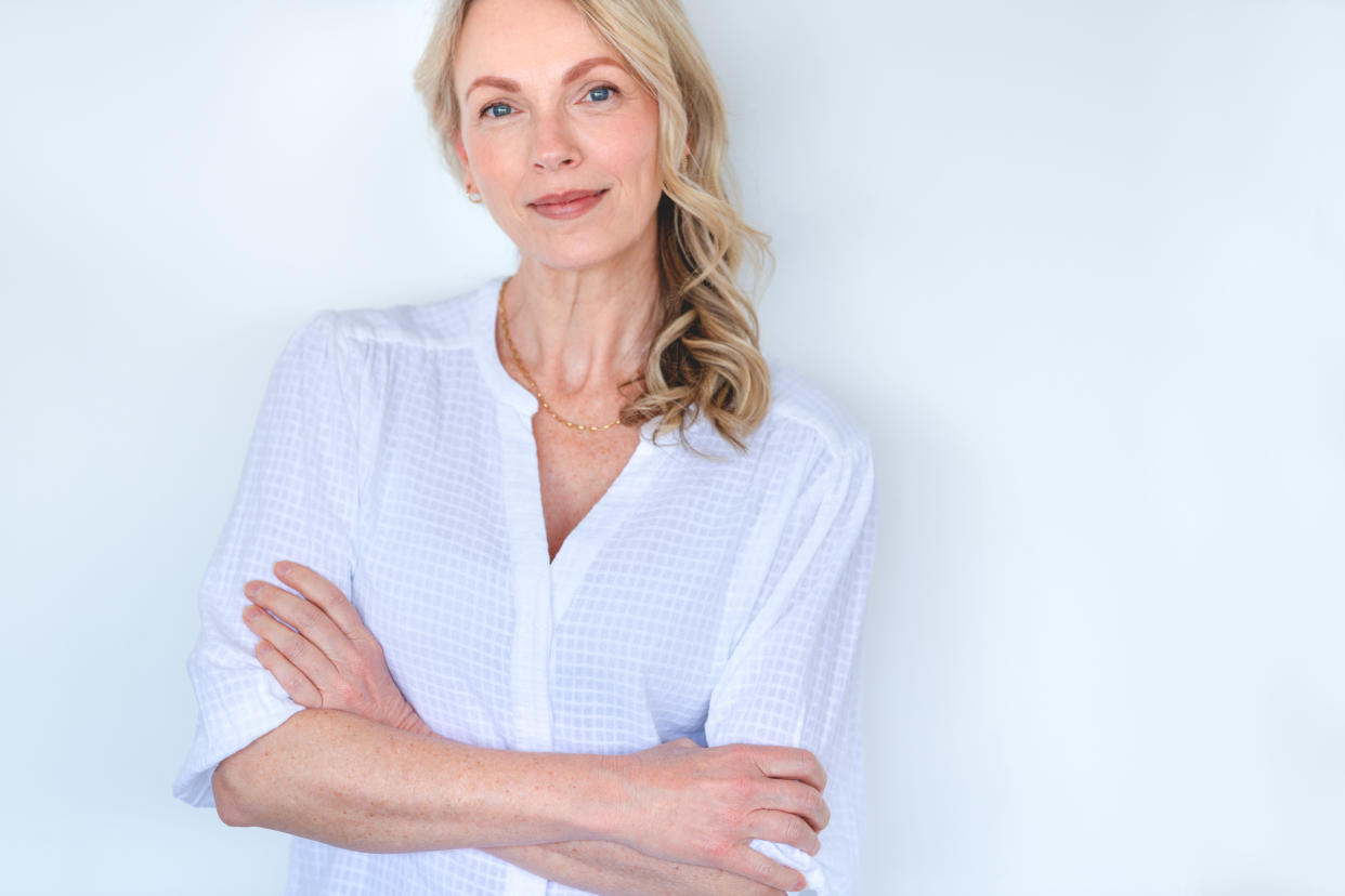 Attractive Mature woman looking strong and confident and relaxing and looking at the camera. She is standing against a white wall with her arms crossed