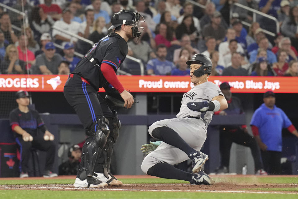 New York Yankees' Aaron Judge scores next to Toronto Blue Jays catcher Danny Jansen on an RBI double by J.D. Davis during the sixth inning of a baseball game Friday, June 28, 2024, in Toronto. (Chris Young/The Canadian Press via AP)