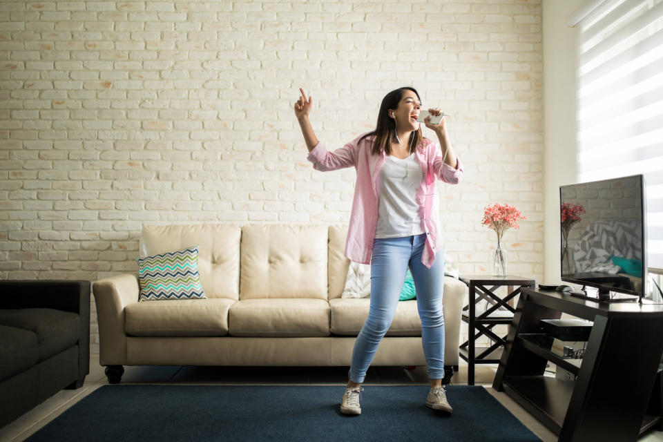 A young woman sings karaoke into her smartphone in her living room.